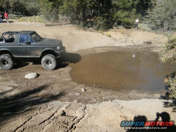 Dark off-road SUV with large tires approaching a muddy puddle on a dirt track