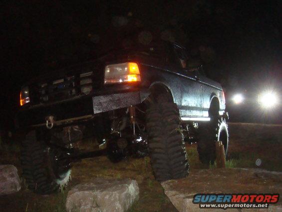 1992 Ford Bronco with large off-road tires and custom bumper on rocks at night
