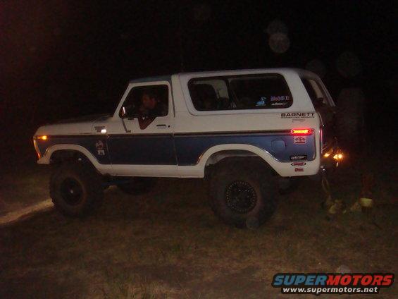 White and blue Ford Bronco with lifted suspension and off-road tires, seen from the side at night