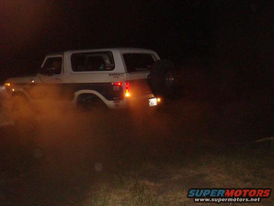 White Ford Bronco with spare tire on rear, kicking up dust at night. Barnet decal visible on side