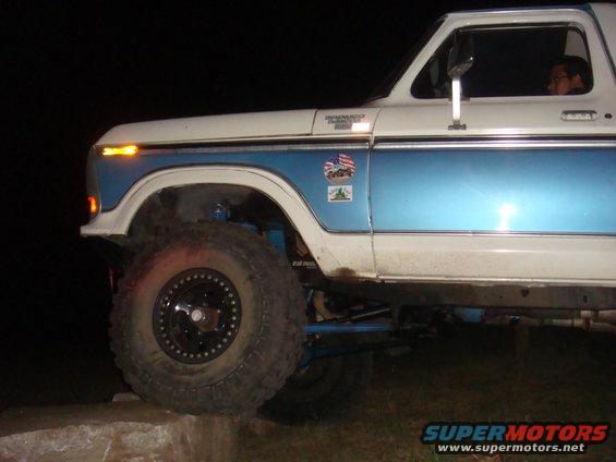 White and blue Ford Bronco with off-road tires, lifted suspension, and American flag sticker