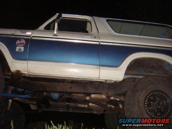 Side view of a lifted Ford Bronco with blue and white paint, showing aftermarket wheels and exhaust
