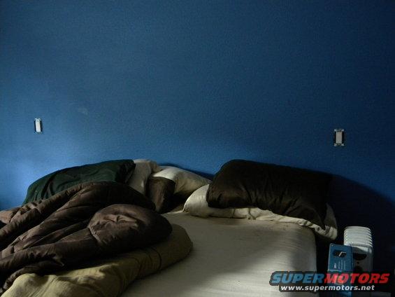 Bed with rumpled brown and green blankets and pillows against a blue wall