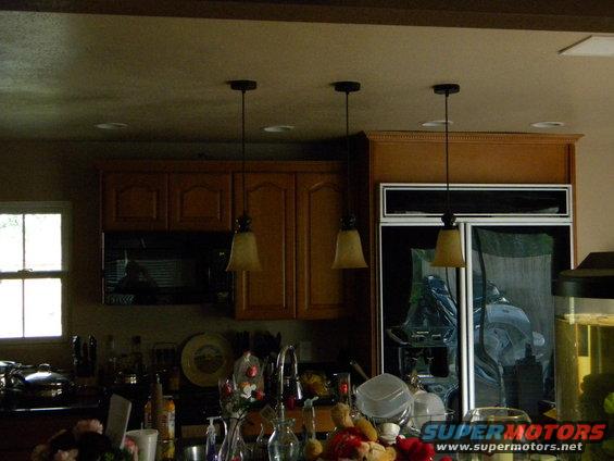Kitchen scene with wood cabinets, refrigerator, sink, and hanging lights
