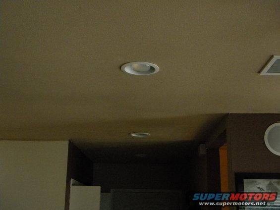 Ceiling with recessed lights and an air vent, with a partial view of a wall and a framed picture
