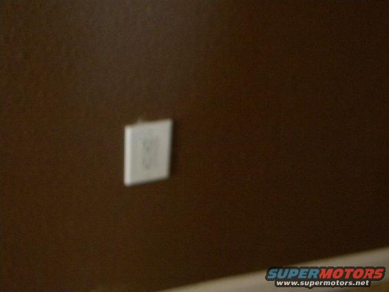 White electrical outlet on brown wall, with Supermotors.net watermark