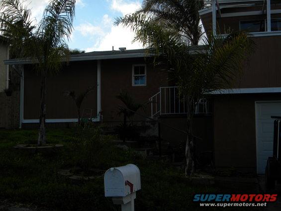 White mailbox in front of a brown house with palm trees and a cloudy sky