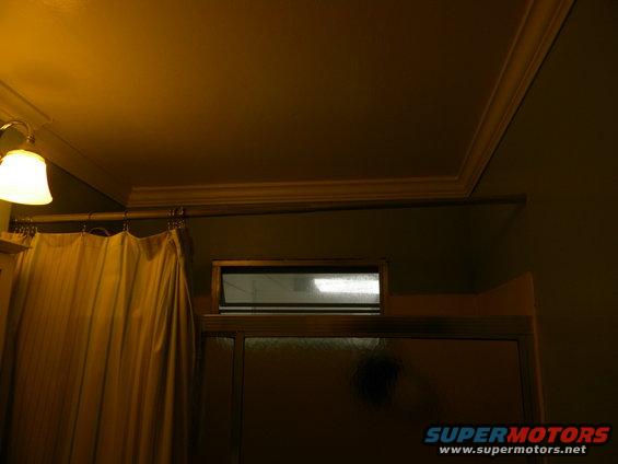 Bathroom interior with shower curtain and small window above shower door. Supermotors logo visible