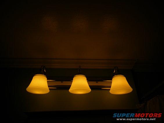 Three yellow pleated lamps hang from a fixture above a dark wall