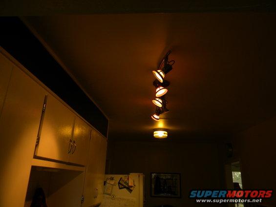 Track lighting on ceiling above kitchen cabinets and a refrigerator