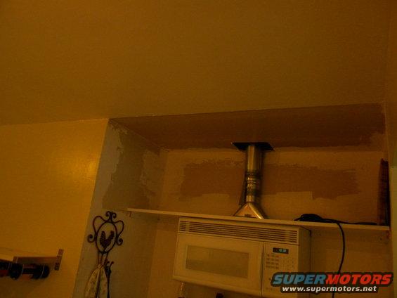 Microwave oven on a shelf with a metal vent pipe above it