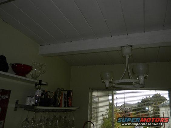 Interior scene with white paneled ceiling, shelves holding glassware and bowls, and a window showing houses and trees