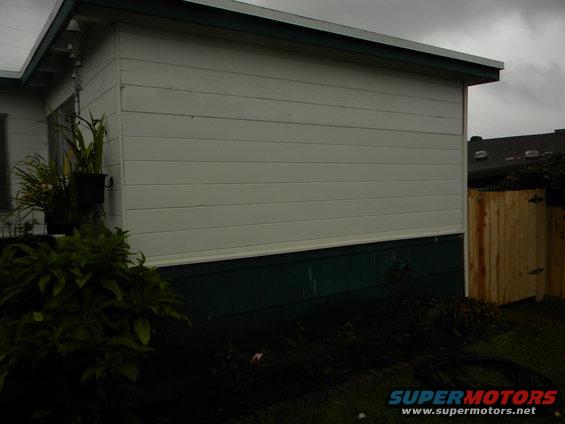Exterior of a house with white siding, dark green foundation, plants, and a wooden fence