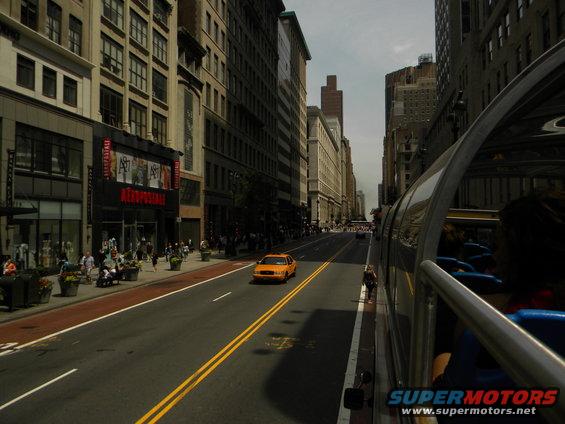 Yellow taxi cab driving on a city street, seen from a tour bus