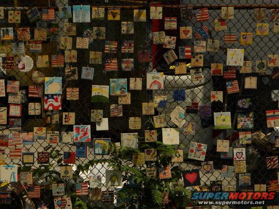 Chain-link fence covered with small, decorated memorial tiles, many American flags