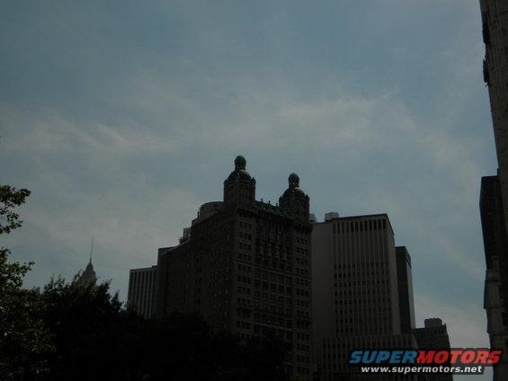 Buildings under a cloudy sky, with a Supermotors.net logo visible