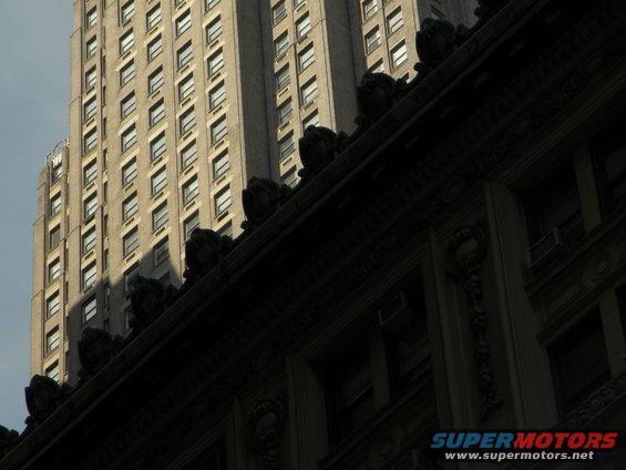 Two tall buildings, one in shadow, with ornate architectural details on the lower one