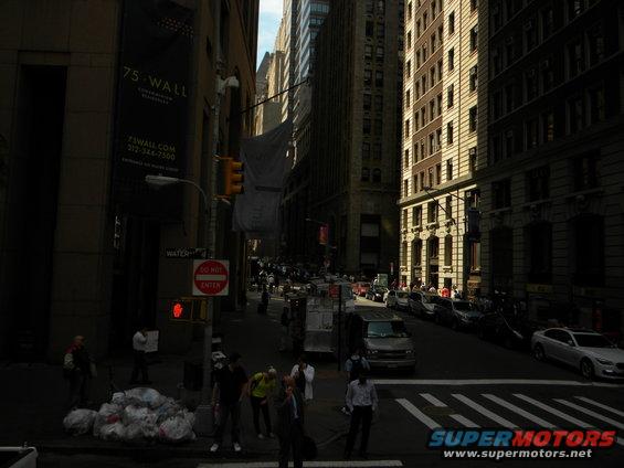 New York City street with tall buildings, traffic, and pedestrians. A banner for 75 Wall Street is visible