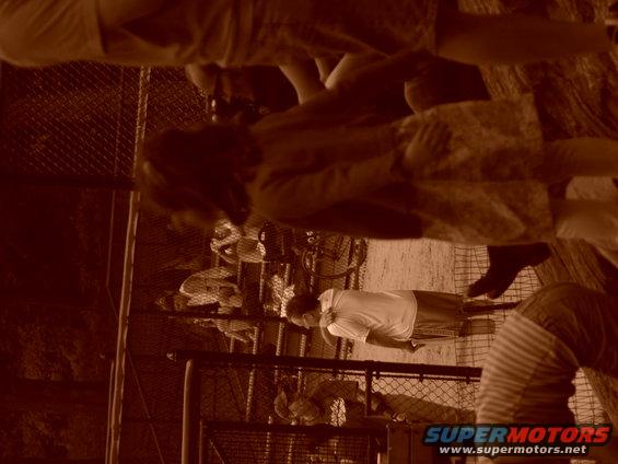 People gathered behind a chain-link fence, some looking down