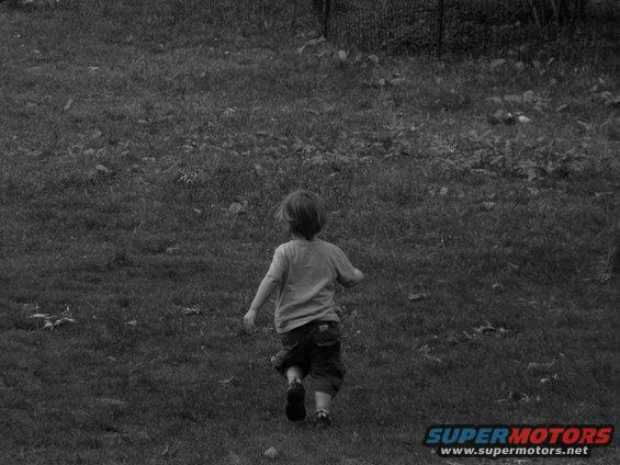 Child running away from camera across a grassy field