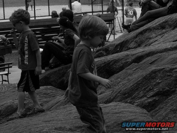 Kids playing on rocks near a bench. One kid wears a Star Wars shirt