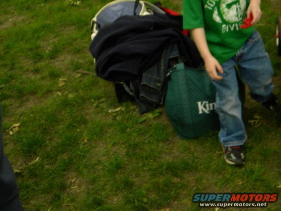 Child in green shirt and jeans standing next to luggage on grass