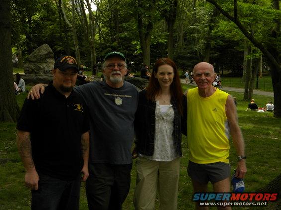 Four people pose for a photo in a park with trees and grass