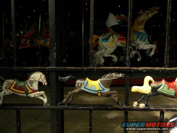 Carousel horses in motion behind a fence. Some have yellow saddles