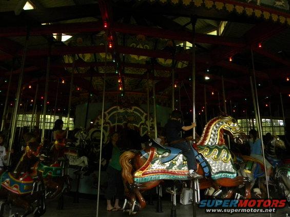 Carousel horses with riders inside a building with lights