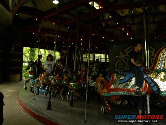 Children ride painted horses on a carousel inside a building with lights