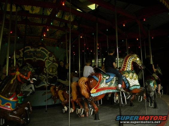 Kids riding carousel horses inside a building with lights