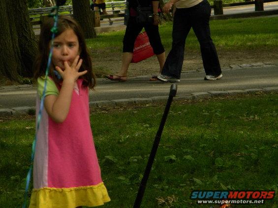 Young girl in a pink and yellow dress stands in a park with people walking in the background