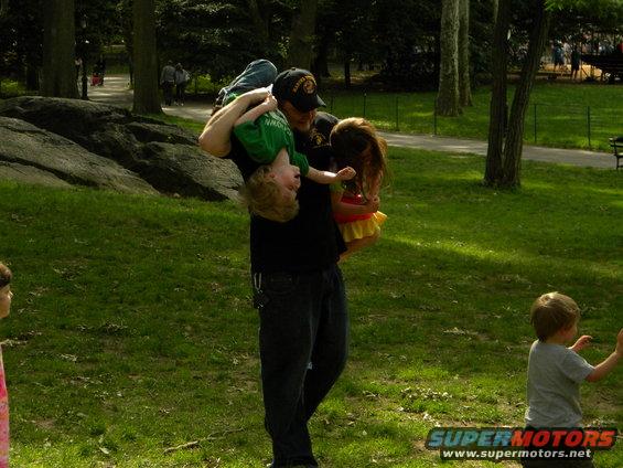 Man carrying two children in a park with a "SUPERMOTORS" watermark