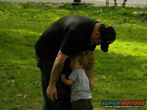Man bending over to hug a small child in a grassy park area