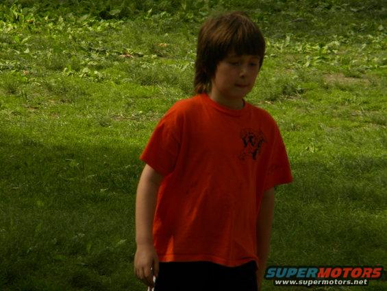 Boy in orange t-shirt and black shorts standing in grass