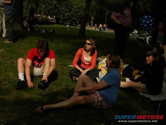 People sitting on grass in a park, with trees and other people in the background
