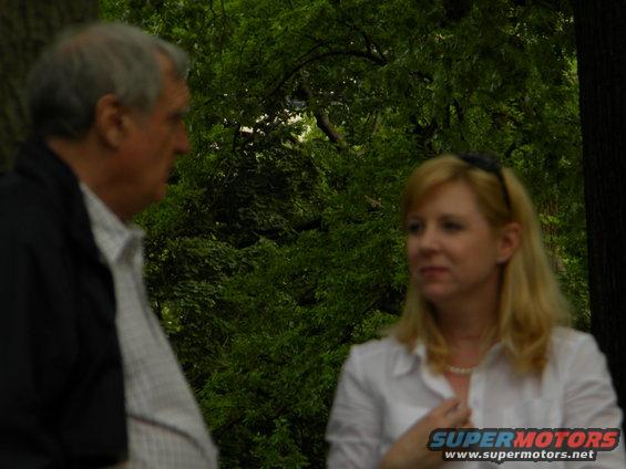 Man and woman talking outdoors with trees in the background. "SUPERMOTORS" logo visible