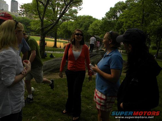 People gathered in a park with trees and buildings in the background