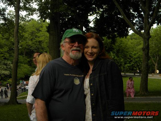 Couple posing in a park with trees and other people in the background
