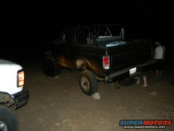Black 1992 Ford Bronco with lifted suspension parked at night, another white vehicle partially visible on the left