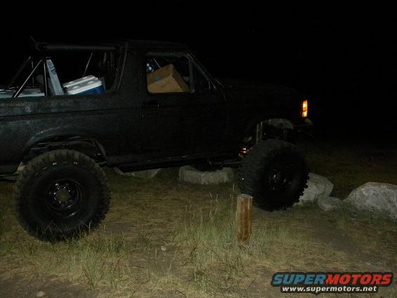 Black 1992 Ford Bronco, modified with large tires and roll cage, parked on uneven terrain at night