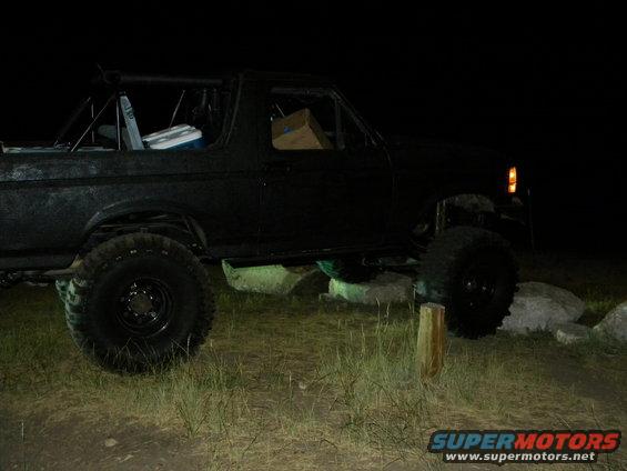 Black off-road SUV with large tires and roll cage, parked on uneven terrain at night