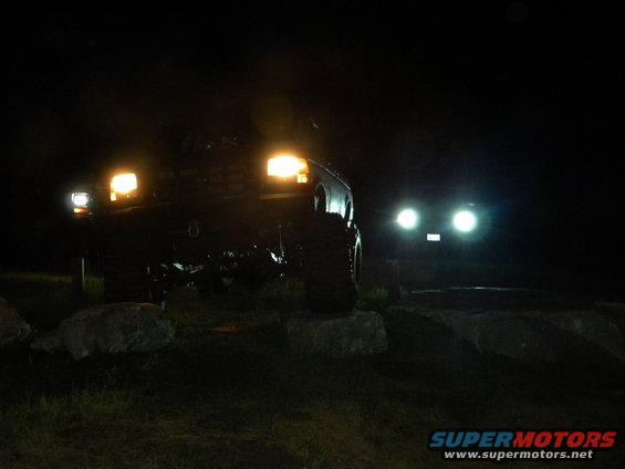 two SUVs with headlights on at night, one in foreground, one in background