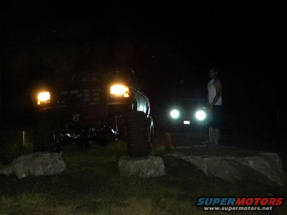 Black 1992 Ford Bronco with headlights on, lifted, on rocks at night