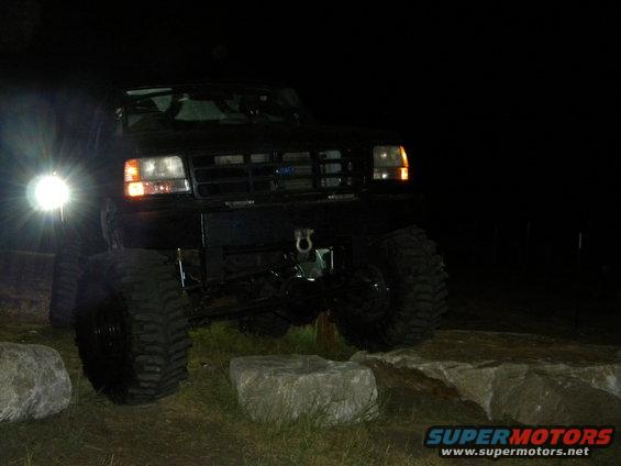 Black 1992 Ford Bronco with large tires on rocks at night, front view