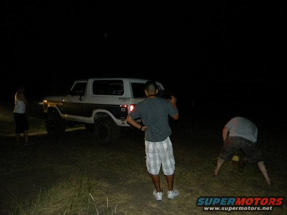 White and brown Ford Bronco with aftermarket wheels, seen at night from a 3/4 front angle