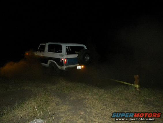 1978 Ford Bronco kicking up dirt at night, spare tire mounted on rear door