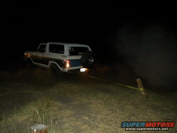 Ford Bronco with spare tire on back, being towed by a strap at night
