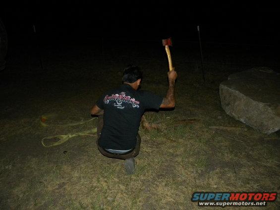 Man crouched in dark holding an axe, with a large rock to the right