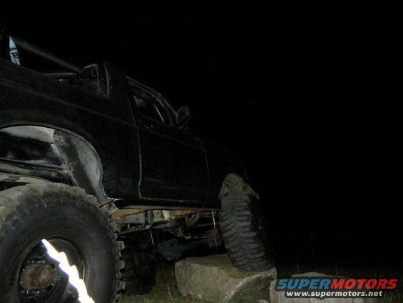 Black SUV with large tires is on rocks at night